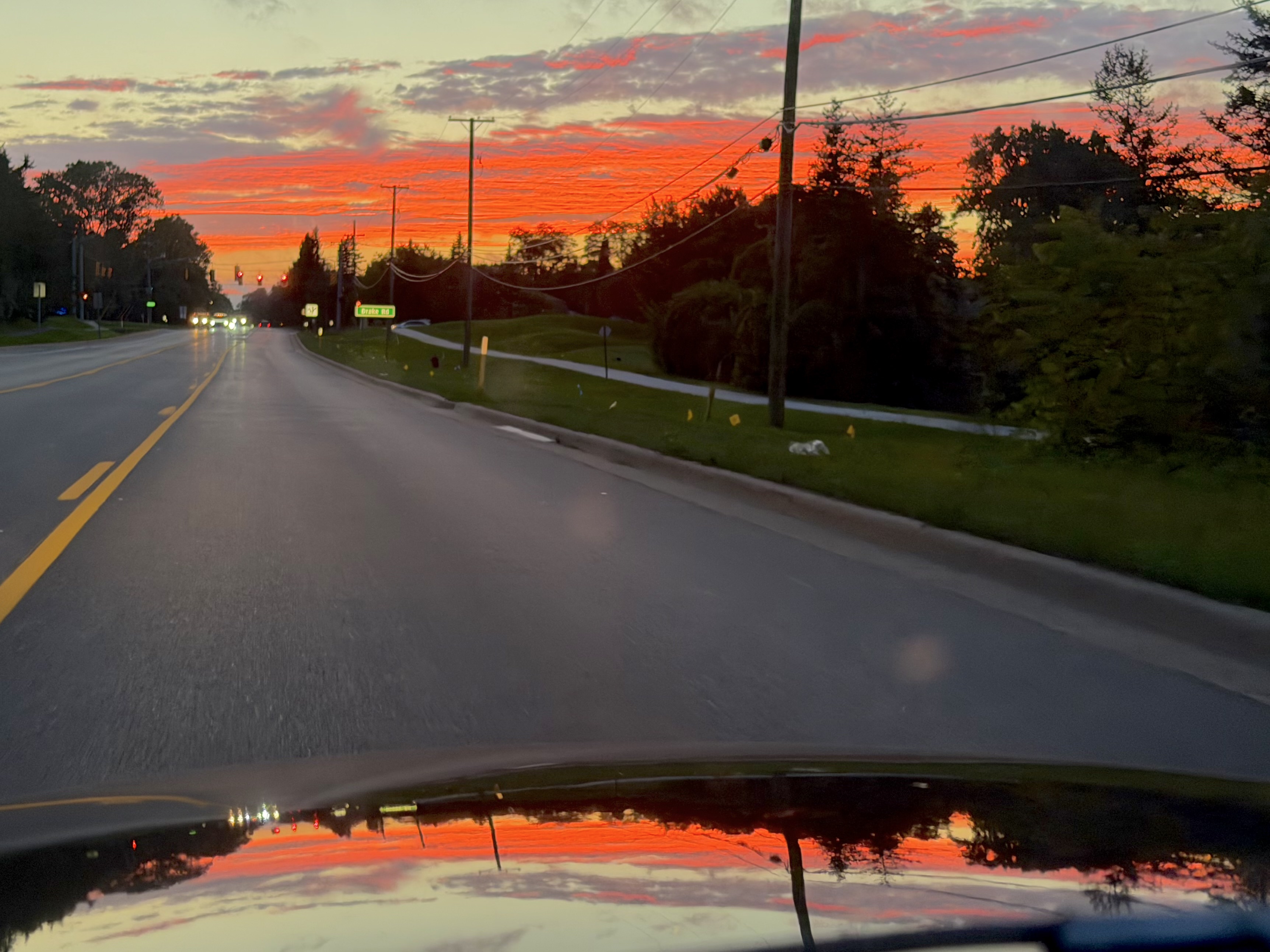Photograph of a bright red sunset along the horizon above a street, reflected in the hood of an MGB at the bottom of the frame.
