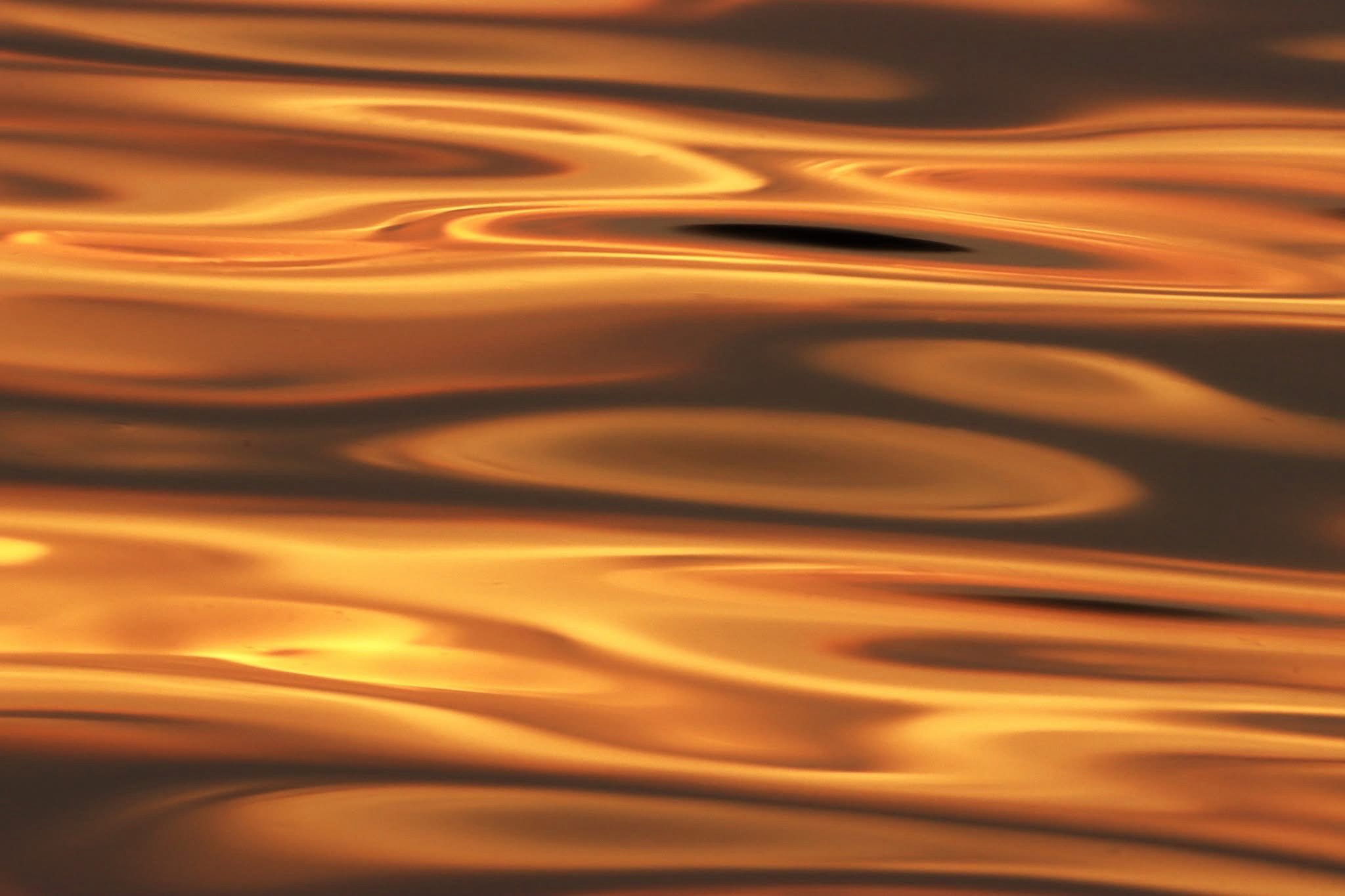 Photograph of Sunset light reflected in a steel lake, forming swirls and horizontal swoops. ￼