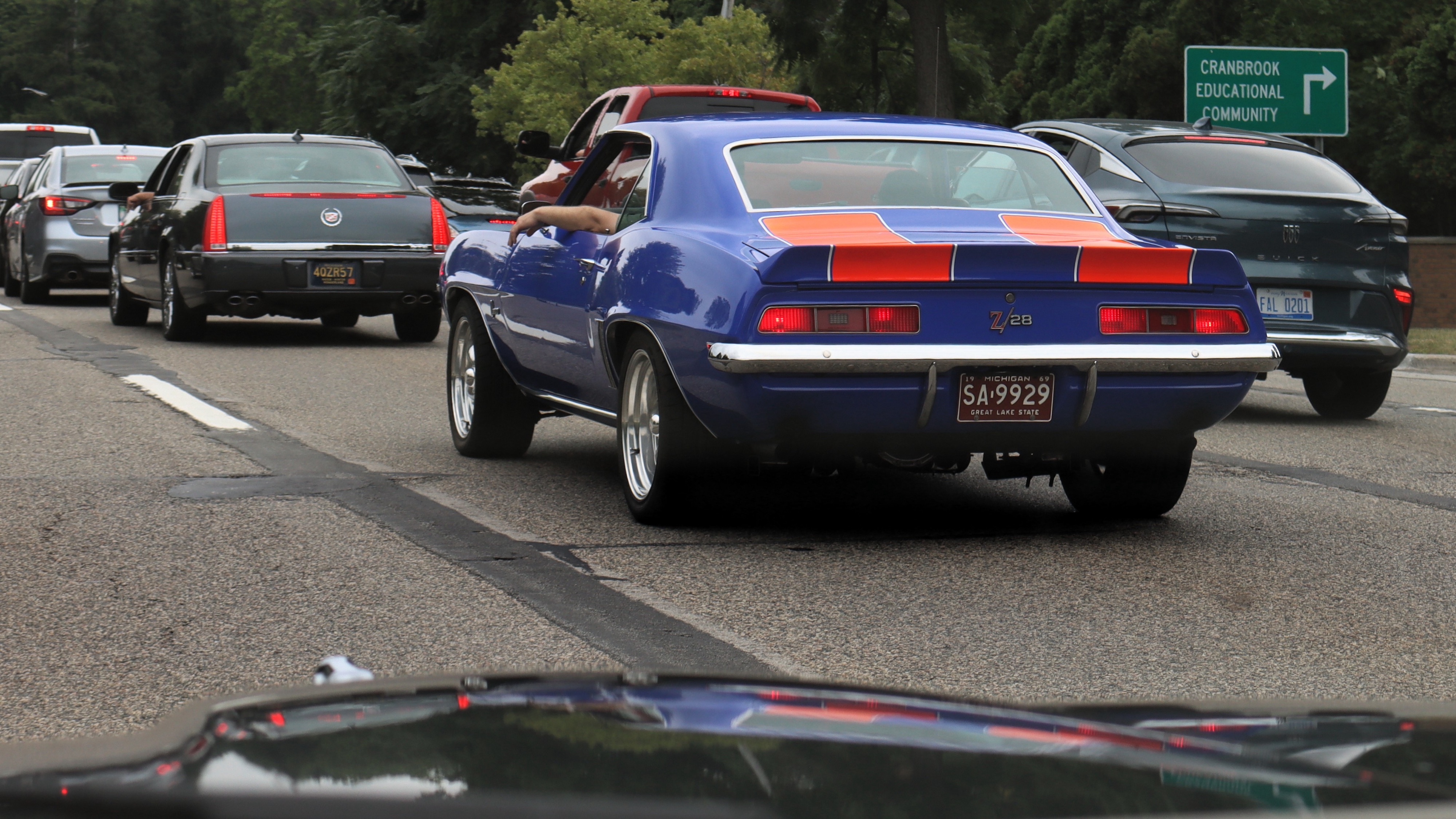 Photograph of an early 1970s blue Chevy Camaro with orange racing stripes in traffic from behind. ￼