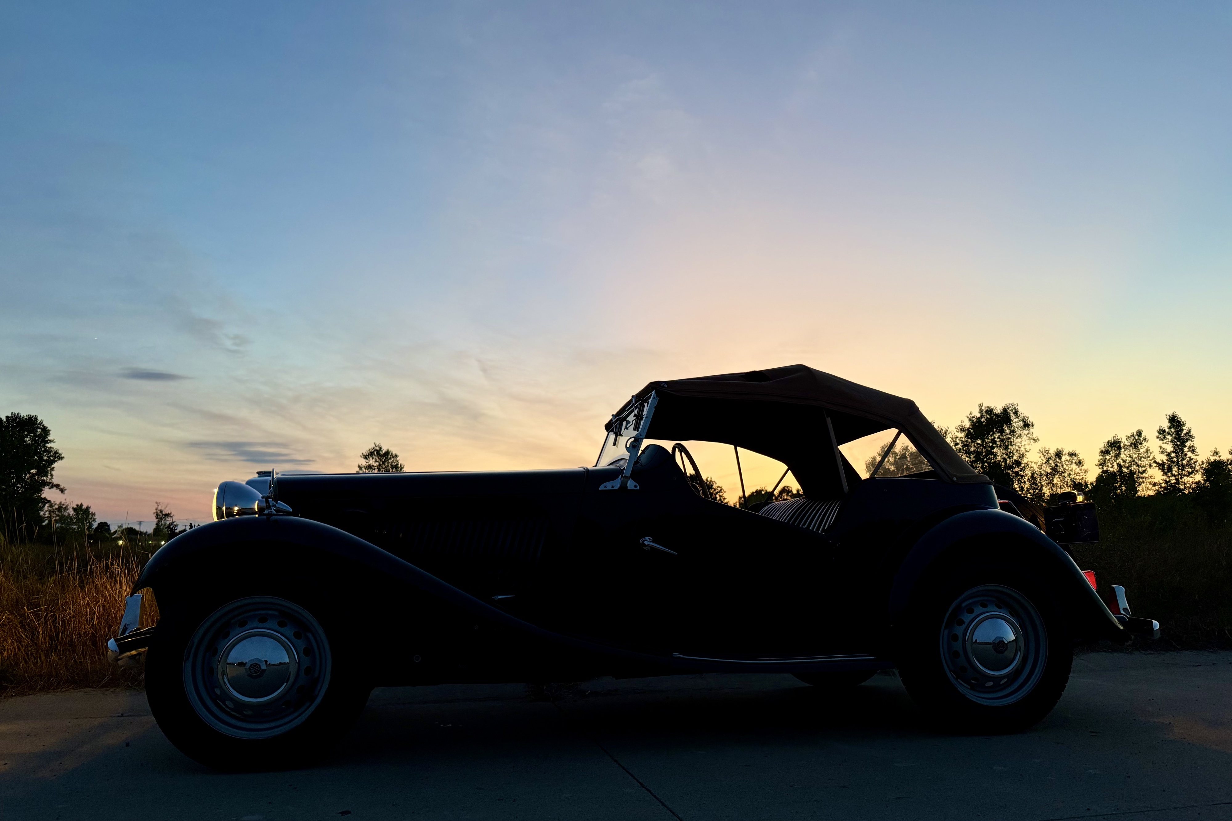 Photograph of a 1950 MGTD seen from the left side in silhouette in front of a fading sunset.