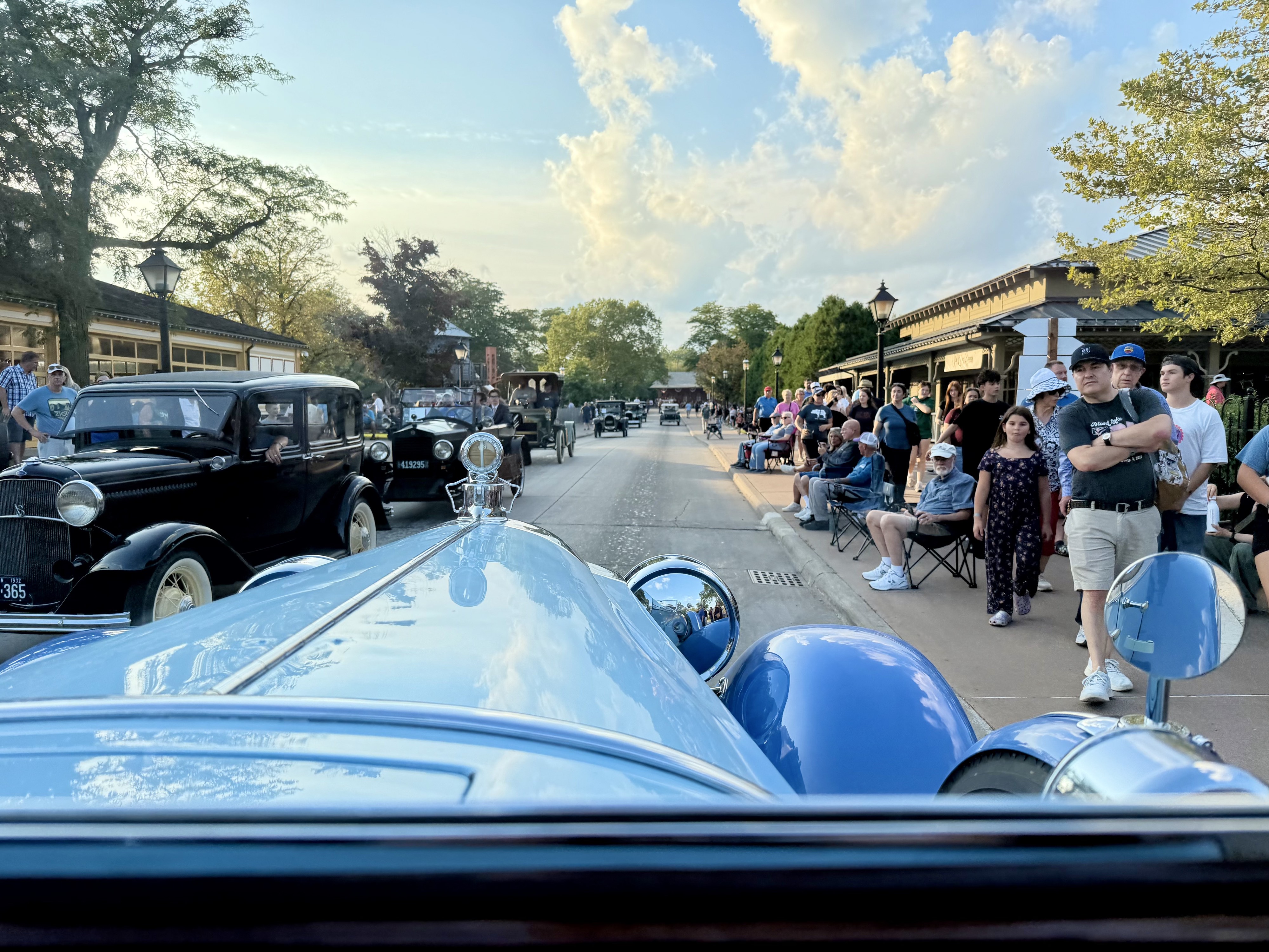 Photograph looking down the hood of a periwinkle blue 1928 Packard dual cowl Phaeton as it drives through Old Car Festival in Greenfield Village, Michigan.