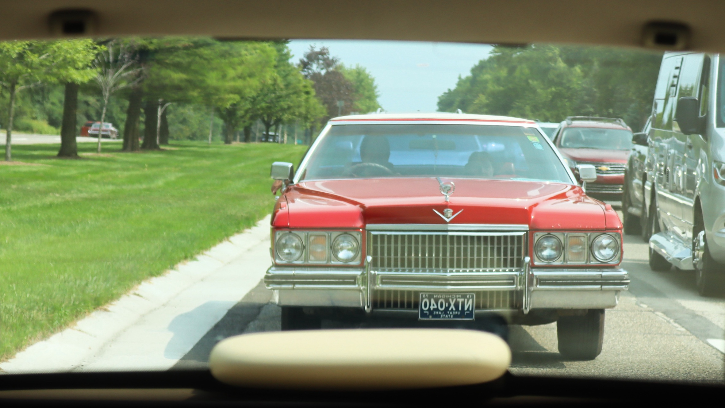 Photograph of a red 1970s Cadillac in a rear-view mirror on a summer day in heavy traffic during the 2026 Dream Cruise.
