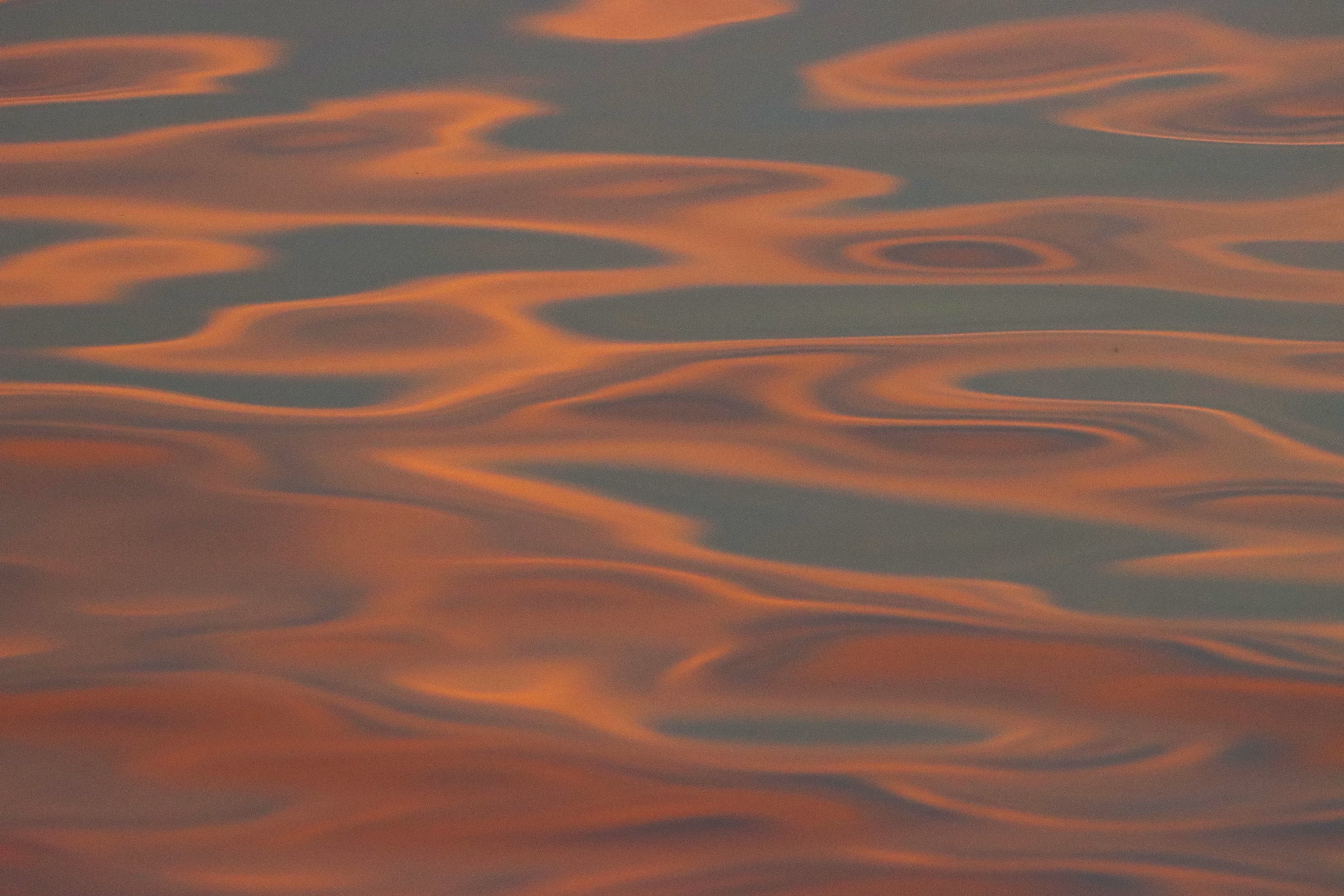 Photograph of sunset, light reflected on water, forming peach and orange swirls against a gray blue background.